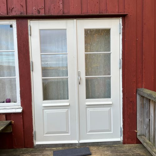 På bildet kan man se en ny, hvit verandadør. Både veggen rundt døra og verandaen bærer preg av slitasje.