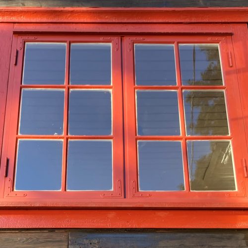 Et bilde av et vindu som har nymalte, røde karmer.