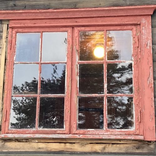 Et bilde av et vindu som har ødelagte karmer. Den røde malinga som er igjen på karmene flasser og er falmet, og det er tydelig at vinduet trenger vedlikehold.