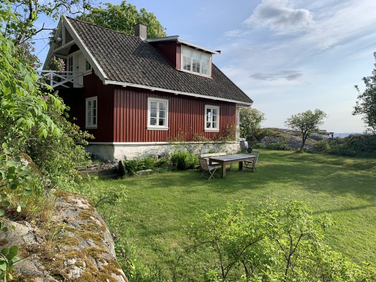 Bildet viser en liten rød stue, som er omringet av en grønn hage.