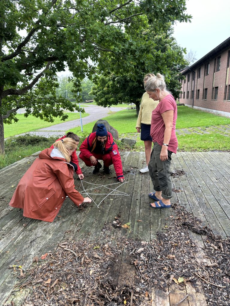 Fire personer er bøyd over fem taustykker på bakken. Taubitene former en stjerne.