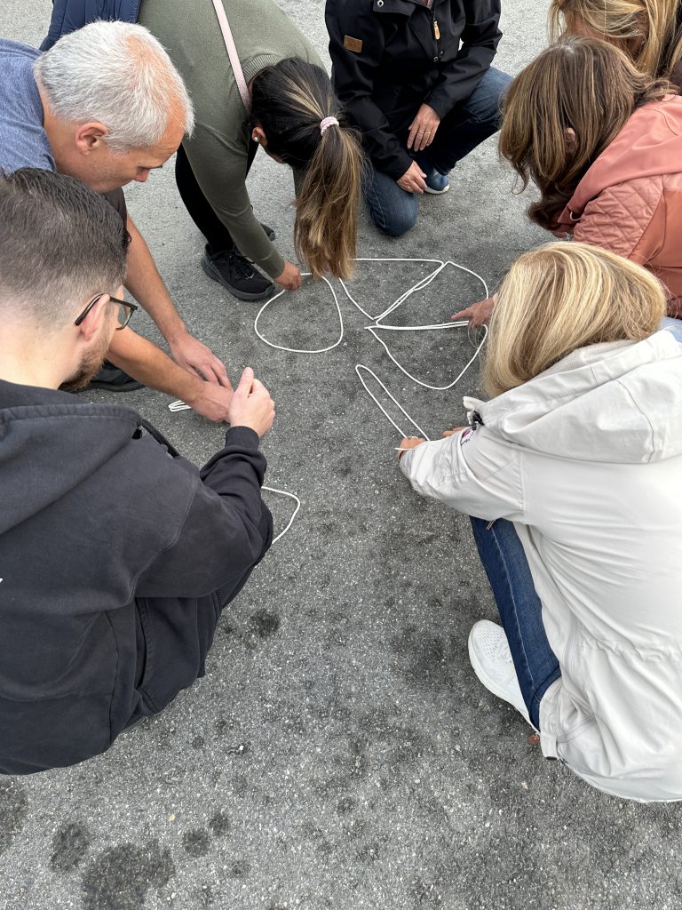 Seks personer sitter bøyd over taustykker som ligger på bakken. Taustykkene er formet som kakestykker i en sirkel.