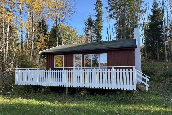 En rød hytte med veranda. I bakgrunnen sees skog.