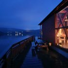 Et bilde av en rød bygning som har et stort vindu ut mot sjøen. Det er lyst inne i bygningen, og mørkt på utsiden.